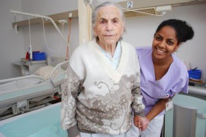 Aufstehen nach der Lehre der MH Kinaesthetics: Die Pflegende unterstützt die Patientin, damit sie ihr Gewicht so bewegen kann, dass ihre Anstrengung niedrig bleibt. Das erspart der Patientin unangenehmes Zerren und der Pflegerin schweres Heben. Foto: khgh.at